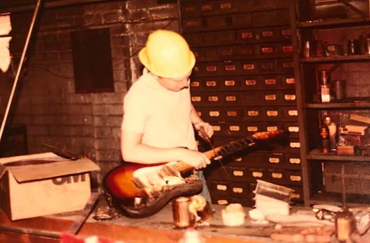 A young John McLaren Jr. in the Fender R&D Model Shop pretending to saw up a burnt Japanese reissue Stratocaster. Picture