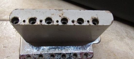 Tremolo block of a 1961 Stratocaster. Inside a larger first hole, there was a smaller hole that blocked the string. Many years after Fender came back to the vintage style bridge; the holes that blicked the strings of the new Synchronized Tremolo were deeper than those of the original one, resulting in a less massive block